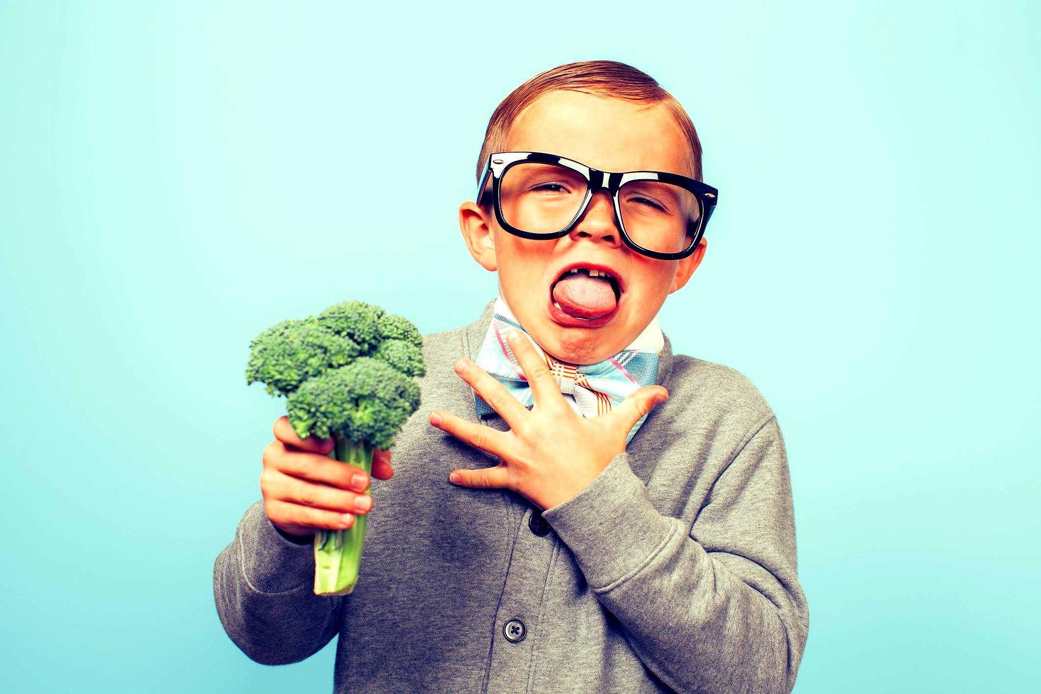 Child with a missing front tooth making a funny face while holding broccoli