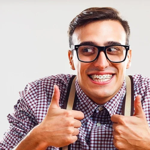 Smiling man wearing traditional metal braces on his teeth and giving two thumbs up