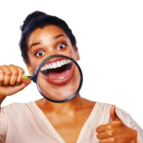 Woman examining her smile with a magnifying glass and giving a thumbs up
