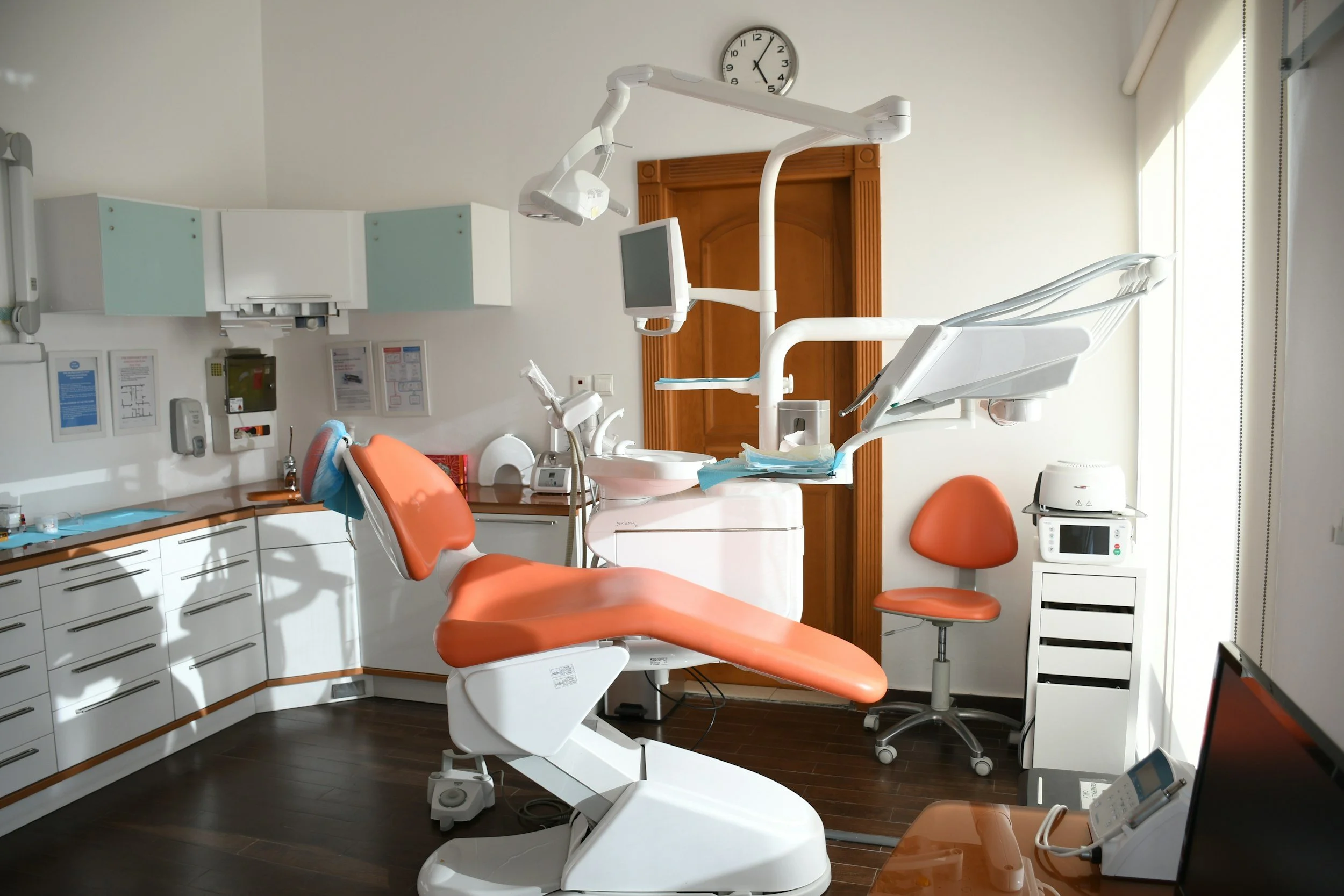Modern dental operatory with dental chair, overhead light, cabinetry, and clinical equipment
